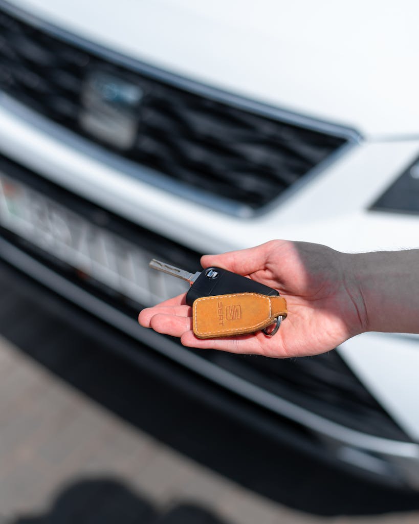 Close-up of a hand holding a car key in front of a white vehicle. Ideal for automotive themes.